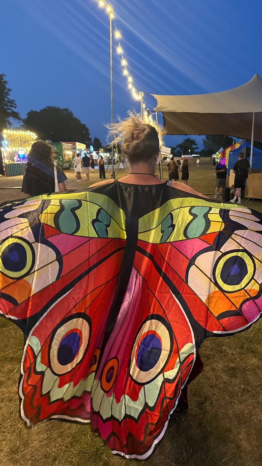 Person wearing a red colorful butterfly cape at an outdoor festival with tents and lights.