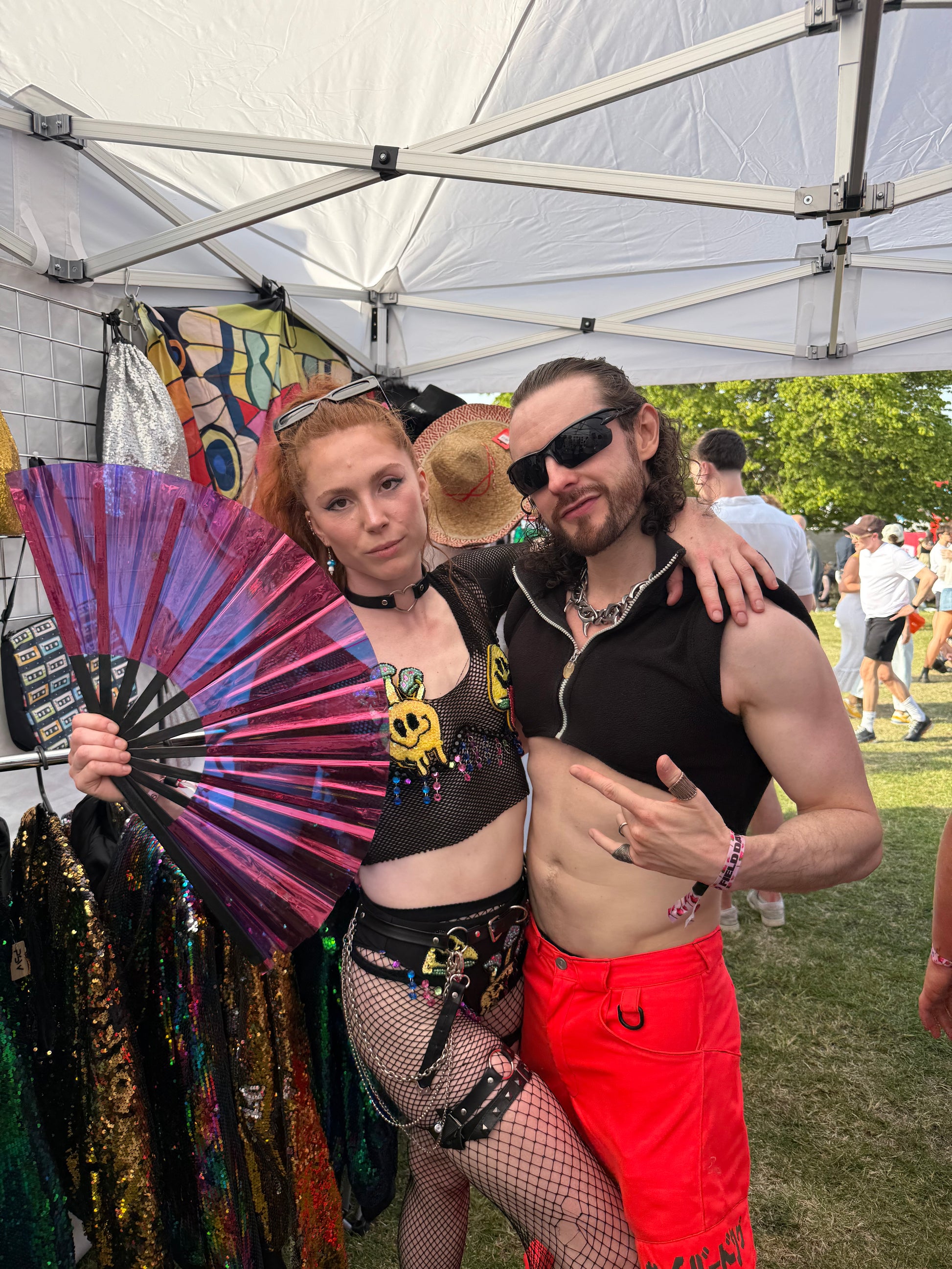 Woman holding a holographic purple folding fan at a festival.