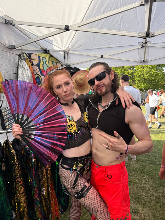 Woman holding a holographic purple folding fan at a festival.