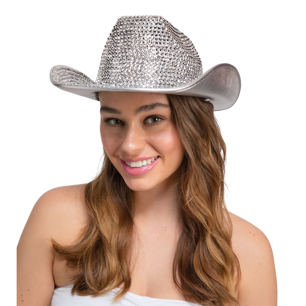 A woman with long wavy brown hair wearing a silver cowboy hat embellished with sparkling rhinestones, photographed against a solid white background.